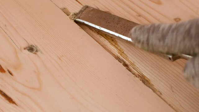 Chisel cleans out old varnish from dent in wooden floor, preparing damaged wood for filling and flawless final coating.
