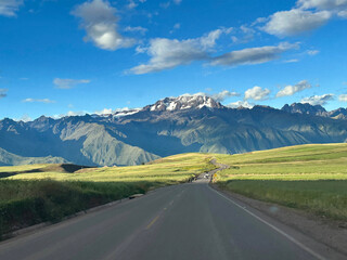 Fototapeta premium A paved road zigzags through the undulations of the terrain, weaving between hills and valleys as it makes its steady ascent toward the rugged mountains of Peru. The black ribbon of asphalt contrasts 