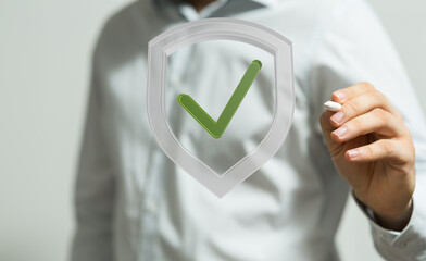 Image of a person drawing a checkmark inside a shield.  Represents security, approval, and data...