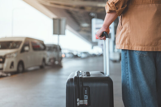 Rear view of male traveler standing with suitcase waiting for taxi at outside airport &ndash; travel concept, transportation and beginning of journey, copy space