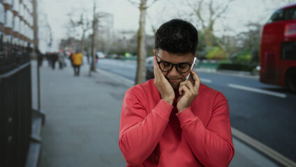 Fototapeta premium Young man in red sweater talking on phone in a city street with red double-decker buses in the background