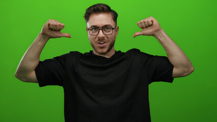 Fototapeta premium Caucasian man with glasses and beard pointing at himself against a bright green wall background wearing a black shirt and smiling confidently.