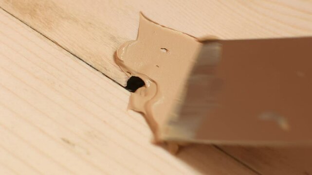 Wood knot cavity is poorly filled with putty, leaving gaps and air pockets, highlighting improper technique in floor repair process.