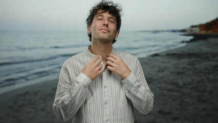 Man wearing white shirt standing on beach with sea in background, expressing calm and confidence,...
