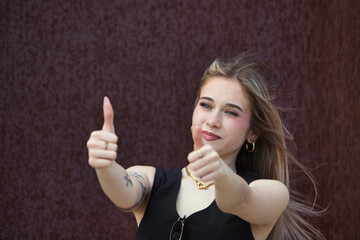 Fototapeta premium blonde woman with light eyes, young and beautiful, holds up the thumb of her two hands and makes a gesture that everything is fine, and it is correct. The woman is happy and smiles.