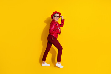 Fototapeta na wymiar Stylish middle aged woman in trendy red outfit posing against vibrant yellow background in a cheerful modern fashion style