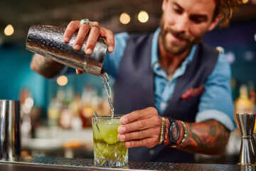 Bartender pouring cocktail with ice cubes using shaker in bar with stylish background lighting