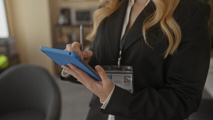 Woman holding tablet in office setting with blonde hair and smart business attire, focusing on task while using stylus for precise input.