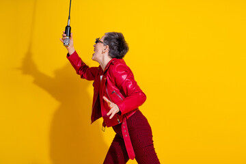 Energetic senior woman singing passionately while holding a microphone wearing stylish fashion...