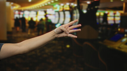 Man showing four fingers with hand extended in vibrant casino setting, surrounded by colorful slot machines indoors, creating lively gambling atmosphere.