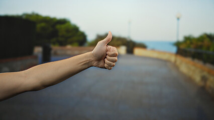 Man showing a thumbs-up gesture with focus on hand against a blurred outdoor city street...