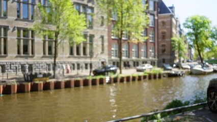 Fototapeta premium Blurred view of amsterdam's iconic canals with vintage architecture and trees reflecting a serene urban atmosphere.