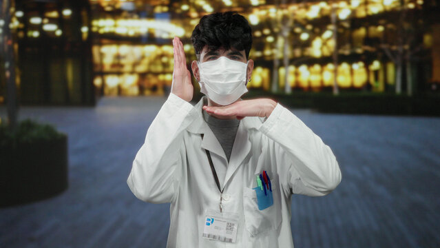 Young man wearing mask and lab coat adjusting his glasses outdoors in an urban evening setting with blurred lights in the background. - Powered by Adobe