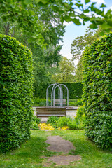 A picturesque garden path leads through tall, green hedges to a bench overlooking a modern water feature. The well-maintained grounds invite you to linger and convey a tranquil, natural atmosphere.