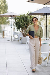 Woman holding laptop and walking on a cafe terrace