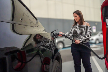 A furious woman holds a charger for her electric car in her hands to refuel her black electric car.