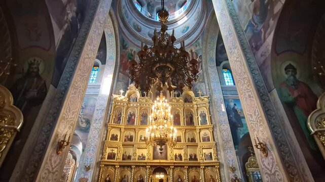 Capriana Monastery indoors view of traditional ornate Christian Orthodox church located in Moldova. Scene during divine service with a monk praying at the altar underneath a grand gilded chandelier
