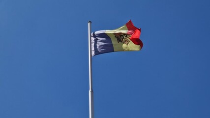 The Moldovan flag flutters proudly beneath a vivid blue sky. Blue, yellow, and red colors and a eagle emblem clutching a cross, a scepter, and an olive branch, signifying heritage and unity of Moldova