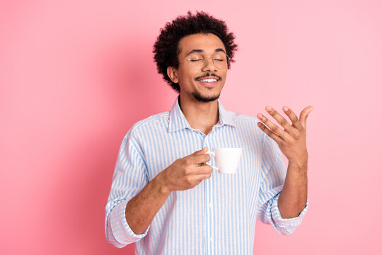 Young man in a striped shirt enjoying a cup of coffee against a pink background expressing happiness and relaxation