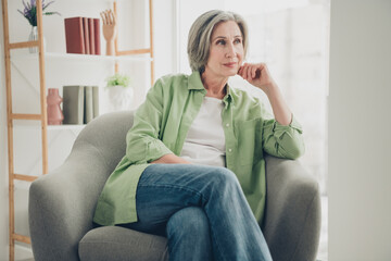 Elderly woman relaxing thoughtfully in a cozy home setting wearing casual attire seated in a comfortable living room armchair