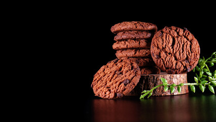 Stack of chocolate cookies on wooden board and decorated with plastic leaves with dark dark background, suitable for advertising and promotion.