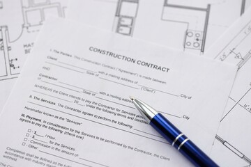 Pen on residential construction agreement and planning blueprints of residential building project