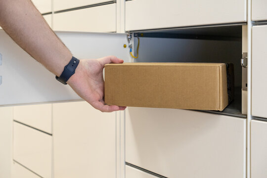 Person retrieving a rectangular cardboard package from a white parcel locker, symbolizing convenient e-commerce pickup and secure delivery services