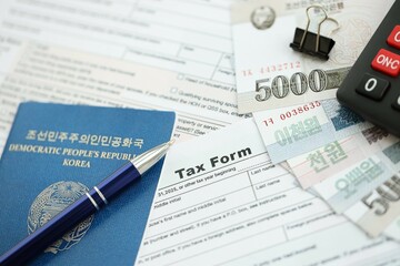 North Korean won money bills lies on table with pen, calculator, passport and tax forms