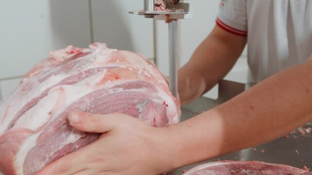 Um a&ccedil;ougueiro cortando um peda&ccedil;o de pernil su&iacute;no em uma bancada de serra de fita no a&ccedil;ougue