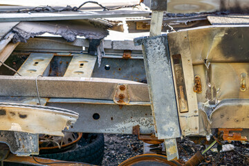 Close-up of a damaged and rusted car frame, showing structural details and burn marks – remains of a destroyed vehicle.