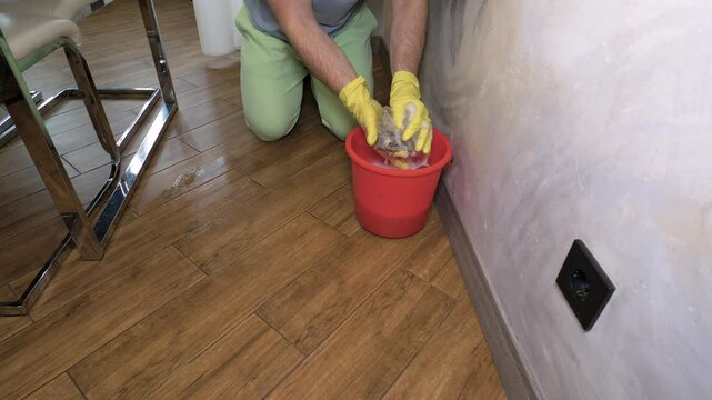 Lifestyle, man washes floor with rag, young man cleans house, wash floor manually with rag with detergent in bucket. Slow motion.