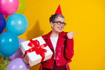Cheerful woman in party setting holding a gift box with red ribbon surrounded by balloons on...