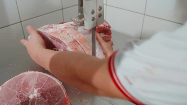 Cena 4k de um pernil su&iacute;no sendo cortado e fatiado em uma bancada de serra de fita por uma a&ccedil;ougueiro