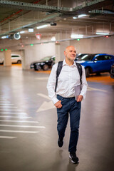 Obraz premium Senior man walking in the park garage and holding a laptop computer in his hand