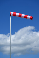 red and white windsock against blue sky and white cumulus clouds