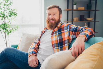 Fototapeta premium Bearded man relaxing in cheerful atmosphere indoors wearing a checkered shirt enjoying a comfortable lifestyle at home