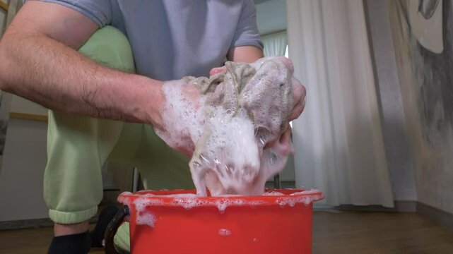 Close-up. A rag in the foam of a detergent. A man washes the floor with his hands with a rag in the foam. A man cleans the house to wash away dirt from the floor. Slow motion.