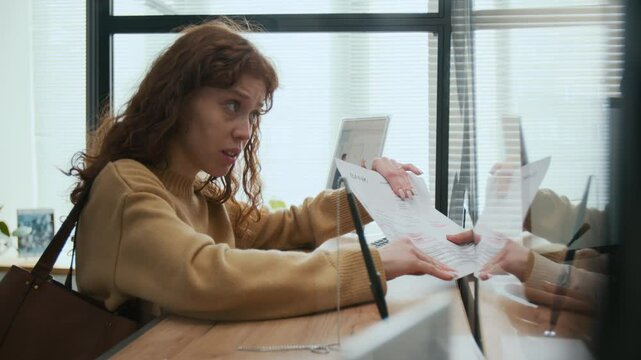 Scandalous woman arguing with Indian bank teller about documents through service window in bank office