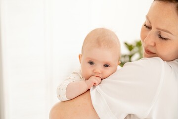 A mother gently kisses and hugs a newborn baby holding him in her arms in a bright bedroom, motherhood or a happy young family with a small child. High quality 4k footage