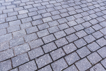 
a gray paving stone consisting of rectangular stone blocks arranged in regular rows in a diagonal pattern.