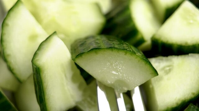 Movement of steel fork with piece of fresh organic cucumber. Vegetable salad ingredient