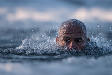 A person is immersed in cold ocean water, splashing droplets as they enjoy a refreshing plunge. The sunrise casts a serene glow, enhancing the revitalizing experience of cold-water bathing