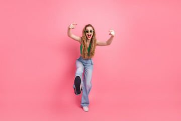 Young woman in green top and jeans posing energetically against a pink background, showcasing a...