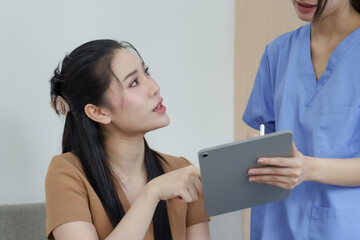 Asian female patient actively discussing dental care plan by pointing at digital tablet while...