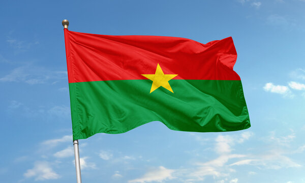 Flag of Burkina Faso with red, green, and yellow star flying in the wind under a blue sky