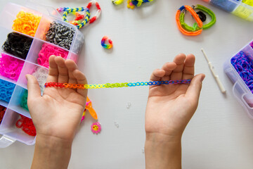 Child's hands crafting colorful rainbow loom bracelet with elastic bands