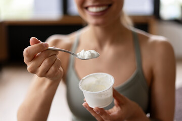 Smiling sportswoman eating yogurt with a spoon after workout selective focus