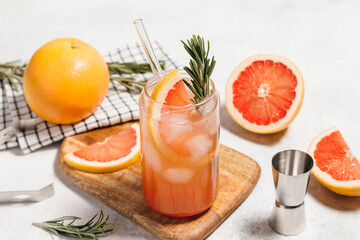 Grapefruit cocktail with rosemary garnish in a glass, served on a wooden cutting board. Vibrant, refreshing drink perfect for summer menu or cocktail recipes. Greyhound, lemonade, paloma, mocktail.