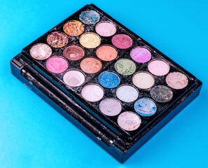 Colorful used eyeshadow palette with powder on blue background