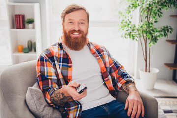 Middle aged man relaxing in a cozy living room with sunlight and modern decor holding a remote control